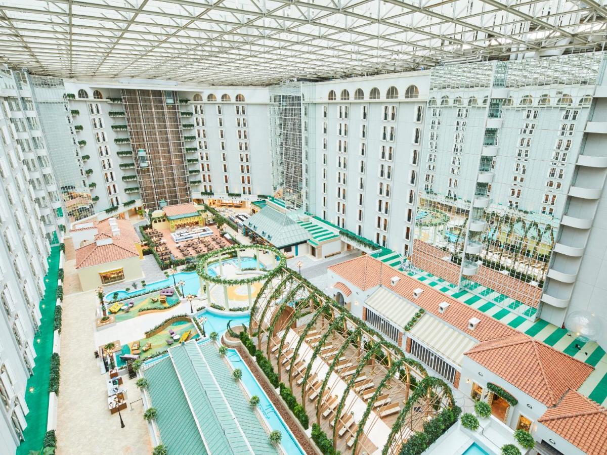 Hotel Grand Nikko Tokyo Bay Maihama Urayasu Esterno foto The photo shows a large indoor space, likely a hotel or resort atrium. The area features multiple levels of buildings surrounding a central courtyard. This courtyard includes various amenities such as pools, landscaped gardens, and recreational areas