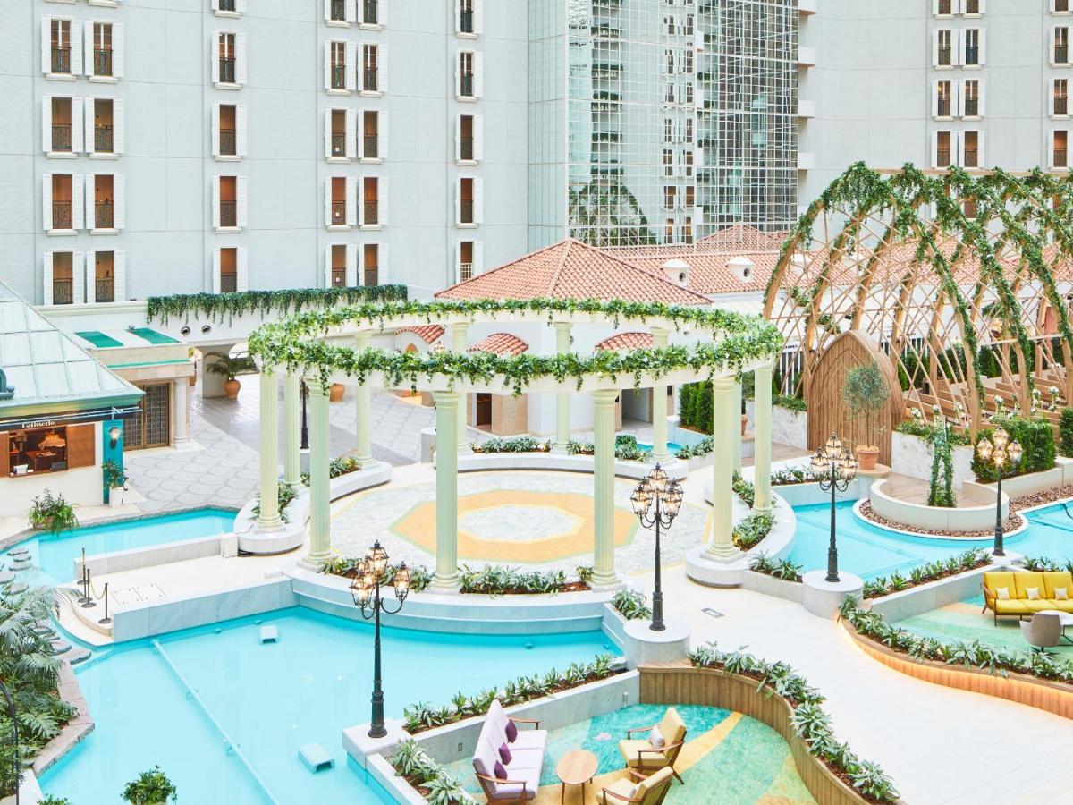 Hotel Grand Nikko Tokyo Bay Maihama Urayasu Esterno foto The photo shows a beautifully landscaped outdoor area, likely part of a resort or hotel. It features a central circular structure supported by white columns, decorated with greenery. Surrounding this structure are several swimming pools or water feat