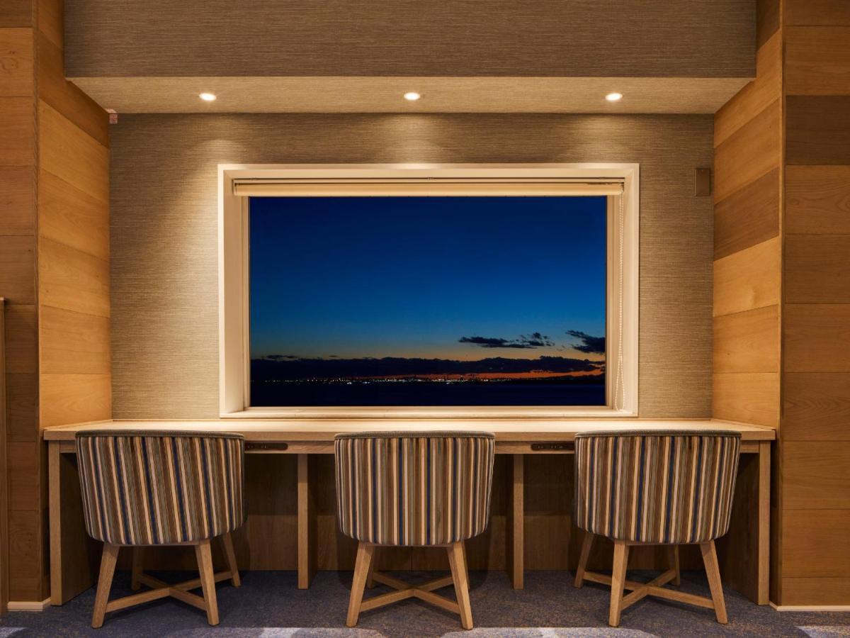 Hotel Grand Nikko Tokyo Bay Maihama Urayasu Esterno foto The photo depicts a cozy workspace or study area featuring a long, minimalist desk with three chairs. The wall behind the desk is made of wood, creating a warm atmosphere. At the center, there is a large window that showcases a beautiful evening view