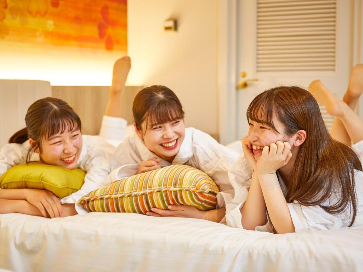 Hotel Grand Nikko Tokyo Bay Maihama Urayasu Esterno foto The photo shows three young women lounging together in a cozy indoor setting. They are dressed in white robes and appear to be relaxed and enjoying each other's company. The women are lying on a bed, with two of them resting on their arms and the thi