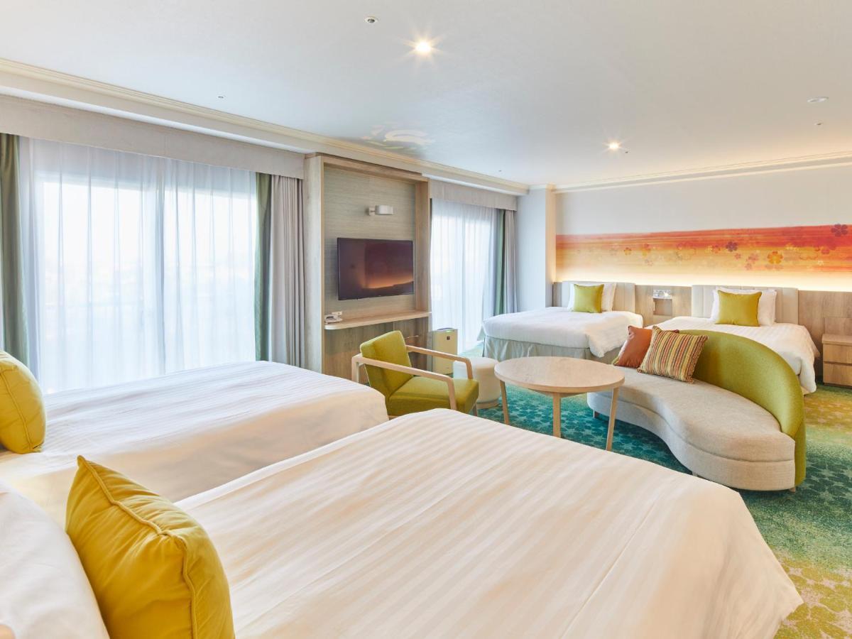 Hotel Grand Nikko Tokyo Bay Maihama Urayasu Esterno foto The photo shows a modern hotel room that features two large beds covered with white bedding and decorative pillows. There is a contemporary, curved sofa in a light color, along with a round table in the middle. The room has large windows that allow n