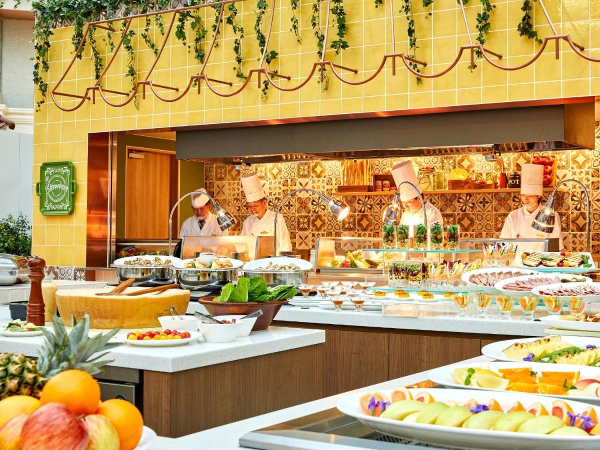Hotel Grand Nikko Tokyo Bay Maihama Urayasu Esterno foto The photo shows a vibrant and colorful buffet setup in a restaurant. In the foreground, there are various dishes arranged on white platters, featuring an assortment of fruits, desserts, and other items. The background features chefs in white uniforms