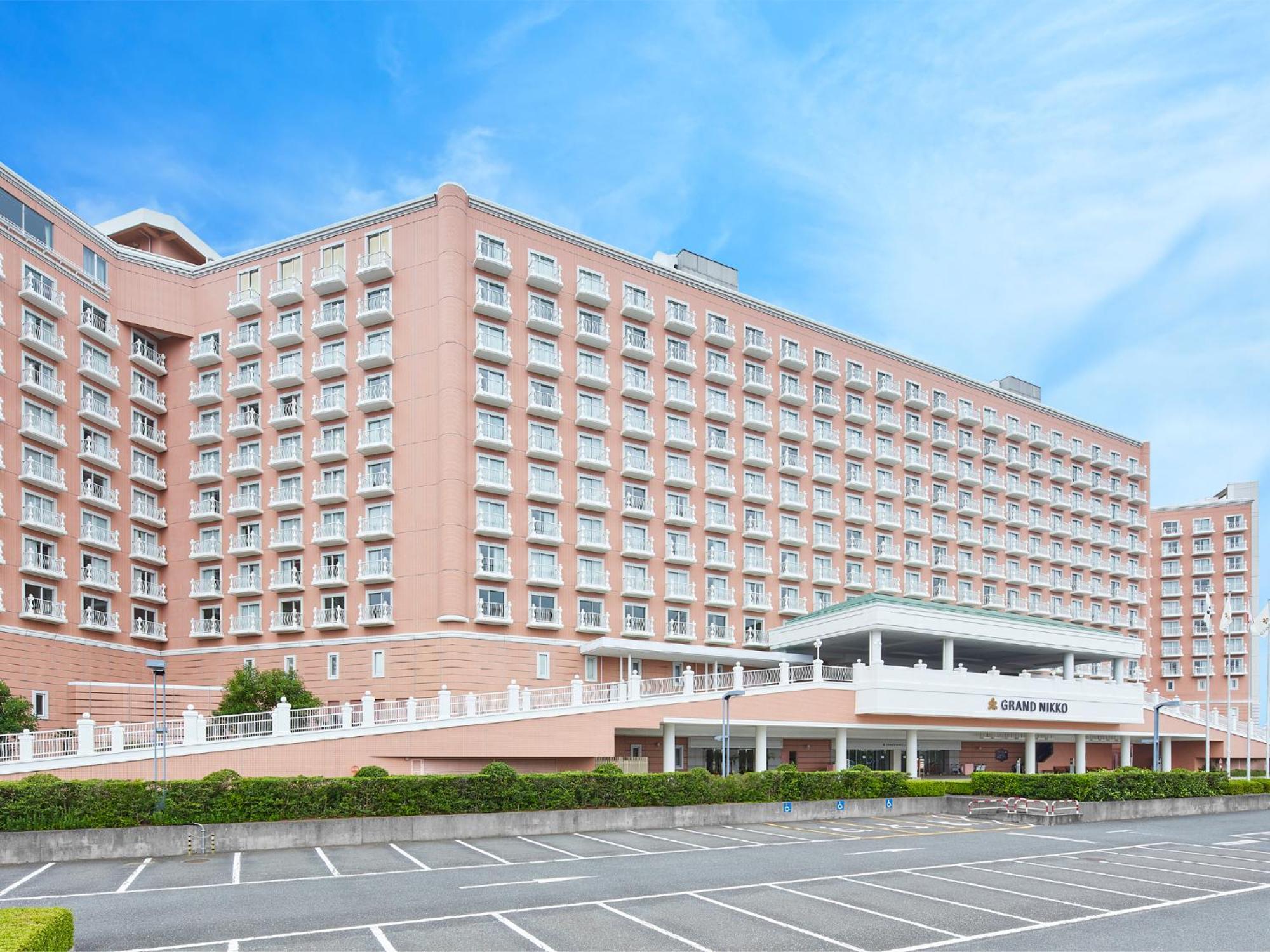 Hotel Grand Nikko Tokyo Bay Maihama Urayasu Esterno foto The photo shows a large, multi-story hotel building, characterized by its pink facade and modern architectural design. The structure features numerous windows and a spacious entrance area, complemented by a canopy. In front of the hotel, there is a p