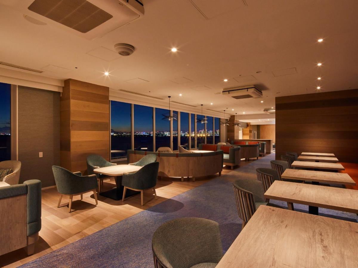 Hotel Grand Nikko Tokyo Bay Maihama Urayasu Esterno foto The photo shows a modern, well-lit lounge or café area. It features a mix of seating options, including cozy armchairs and tables with chairs. The space has large windows displaying a view, likely of a city or landscape at dusk, given the nighttime a