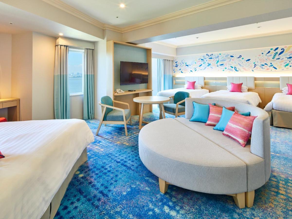 Hotel Grand Nikko Tokyo Bay Maihama Urayasu Esterno foto The photo shows a modern hotel room featuring a spacious layout with multiple beds. There is a large, curved sofa with colorful cushions in the center, adding a contemporary touch to the design. The room has large windows allowing natural light to fi