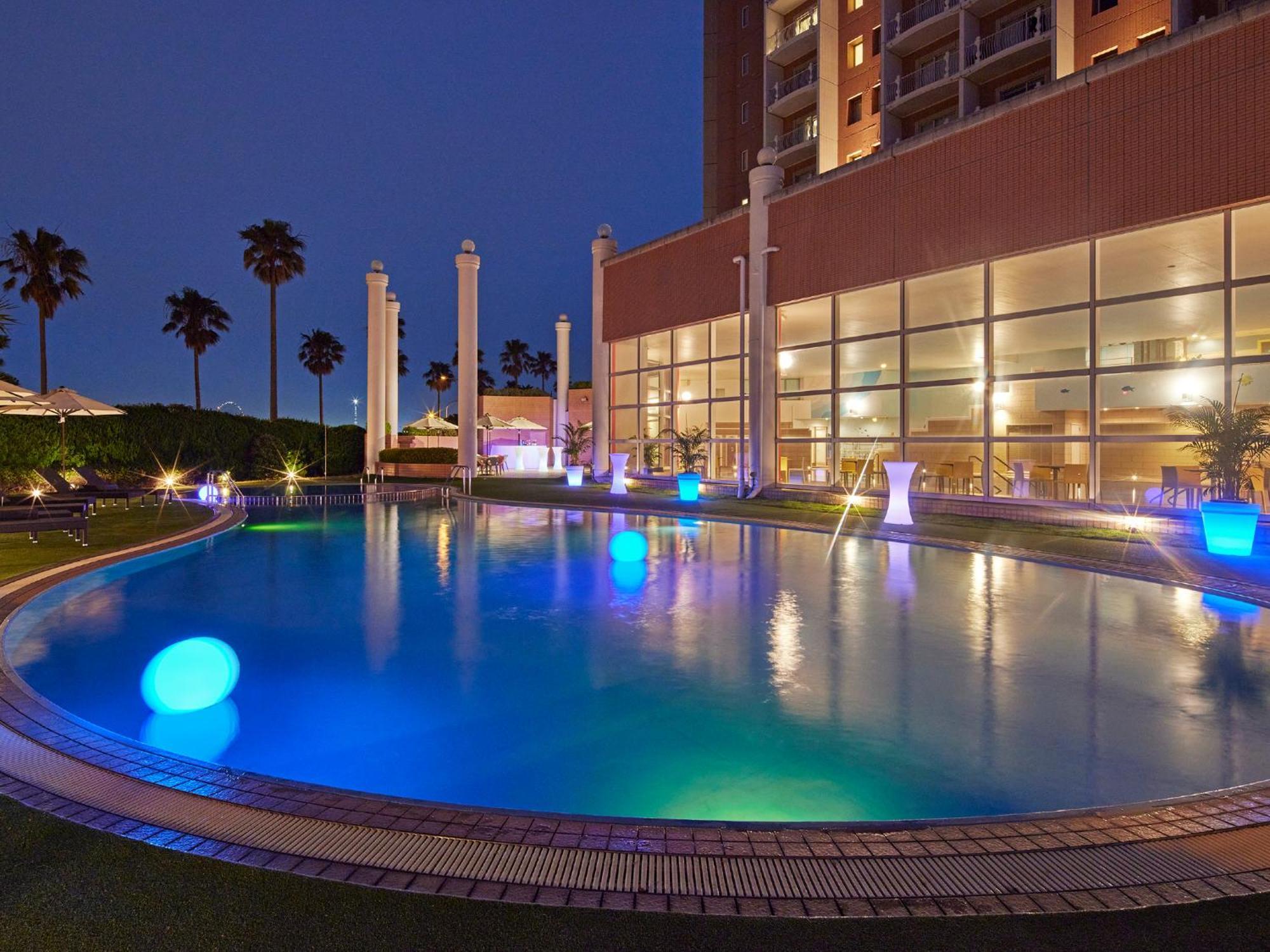 Hotel Grand Nikko Tokyo Bay Maihama Urayasu Esterno foto The photo shows a well-lit swimming pool at night, surrounded by a lush green area. The pool features glowing blue lights that create a serene and inviting atmosphere. Palm trees can be seen in the background, adding a tropical feel to the scene. Add